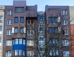 Mehrfamilienhaus in Berlin-Mitte, dunkle Außenfassade, blauer Himmel, viele Fenster