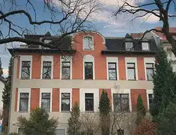 Wohn- und Geschäftshaus in Steglitz-Zehlendorf, rote Außenfassade mit hohen Fenstern und Bäumen vor dem Haus