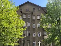 Wohn- und Geschäftshaus in Berlin-Prenzlauer Berg, dunkle Außenfassade, viele Fenster, grüne Bäume vor dem Haus